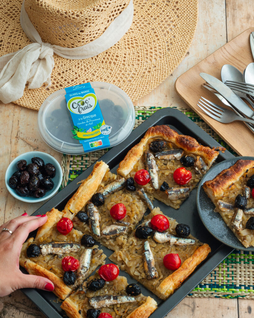 Main qui prend une part de pissaladière avec des olives