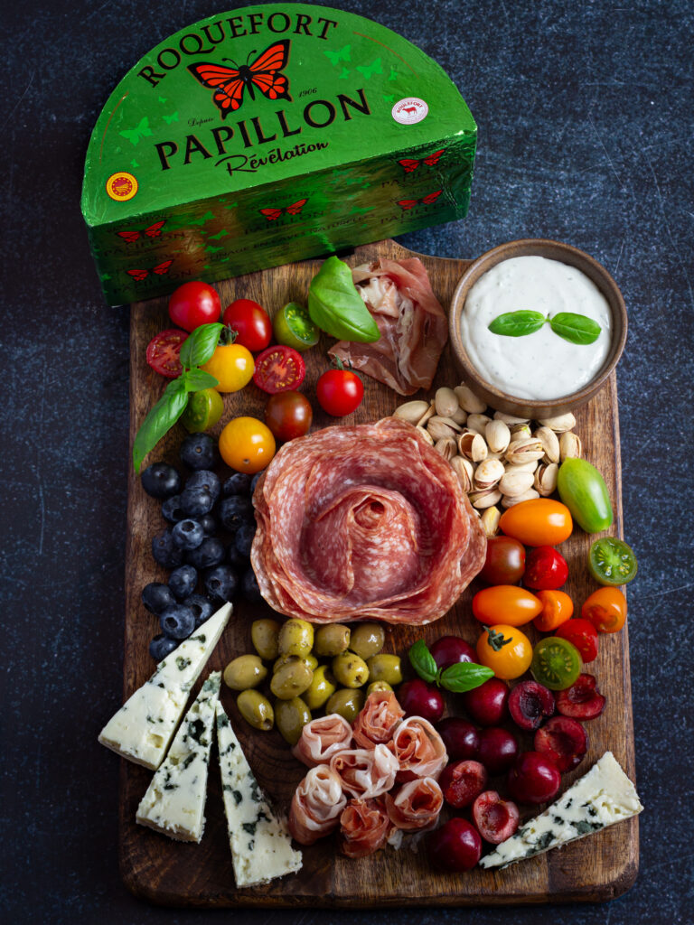 Planche apéritive gourmande avec charcuterie, fruits, fromage roquefort papillon